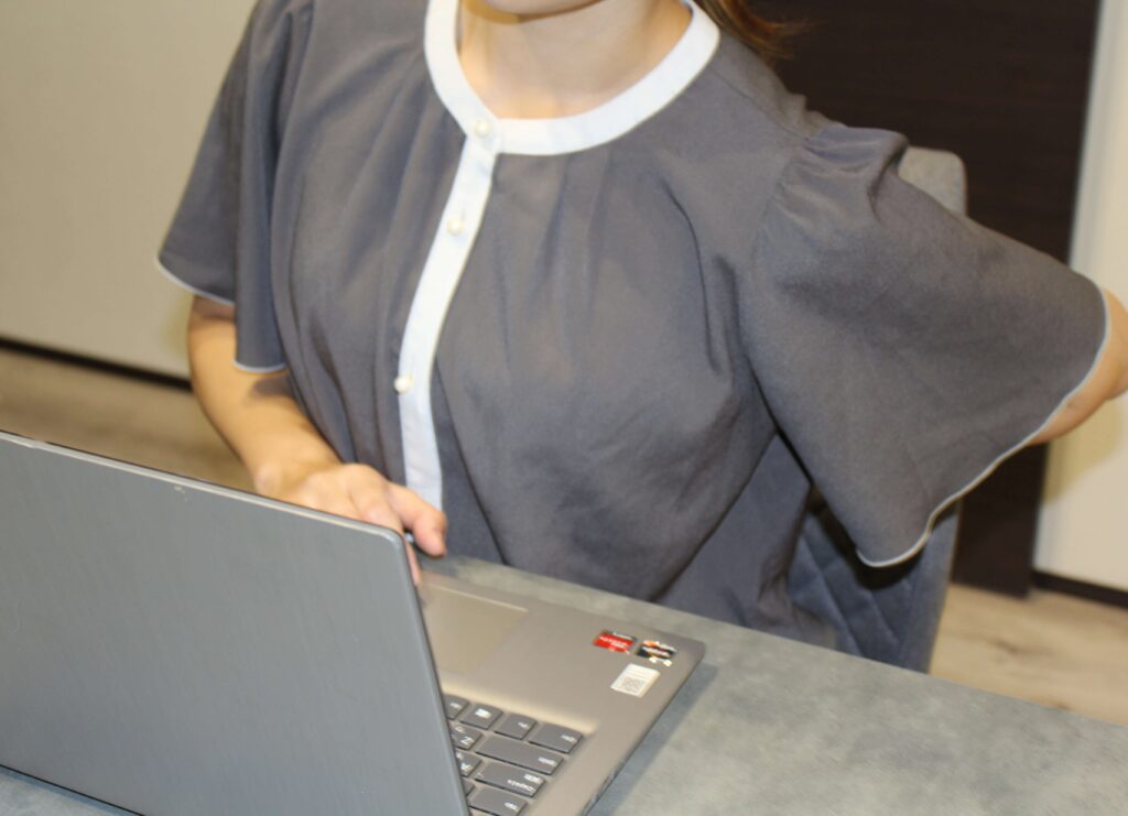 デスクワークをしている女性従業員が生理痛による腹痛と腰痛で悩んでいる写真